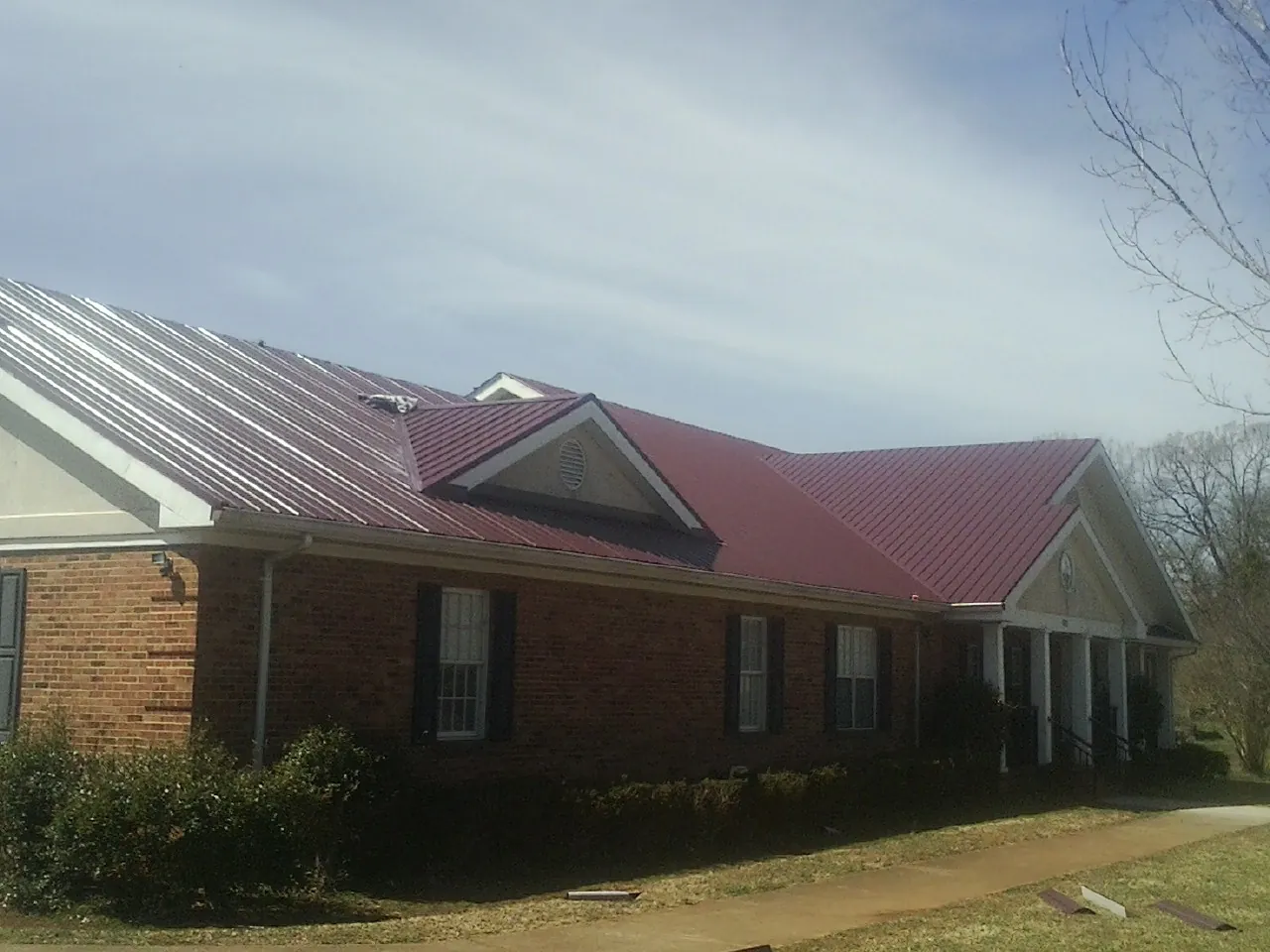 Red metal roof with gabled entries on a long brick building, from a Hail Damage Roof Repair job in Camden